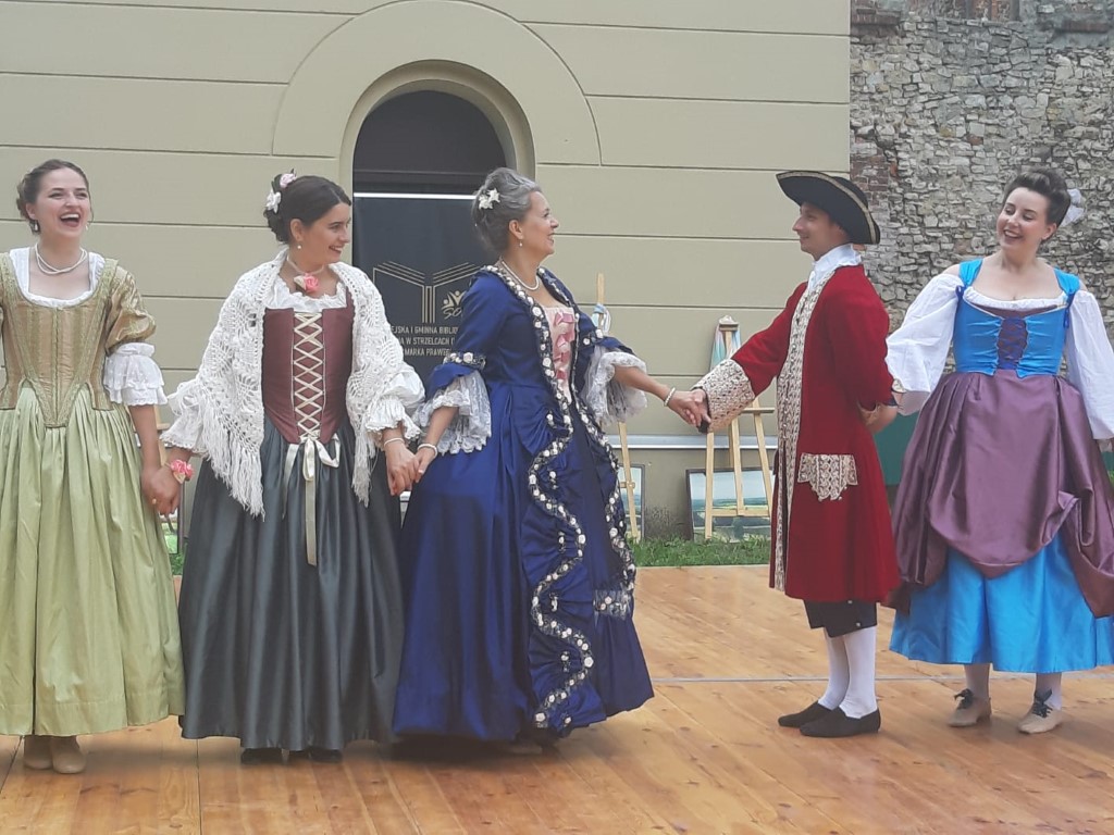 Ludzie przebrani w stroje z epoki barokowej tańczą na scenie.